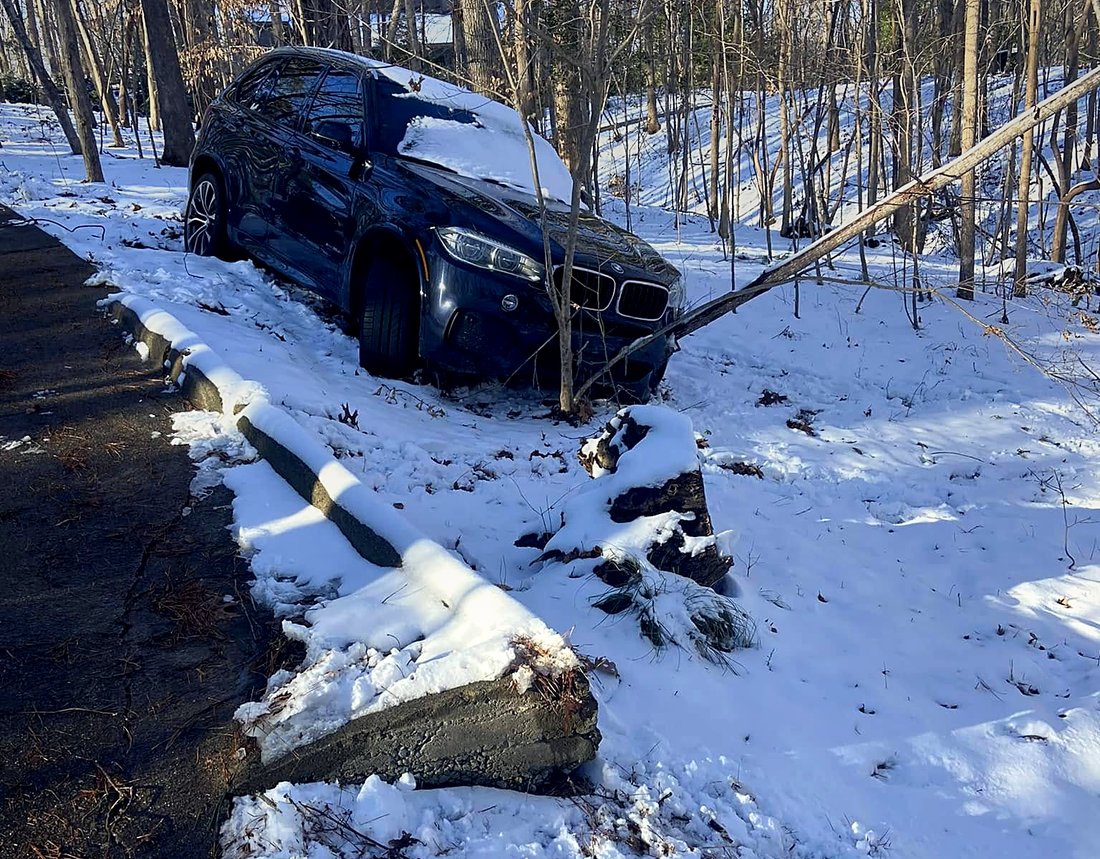 A dark SUV off the road in deep snow, stopped against trees on a wooded bank