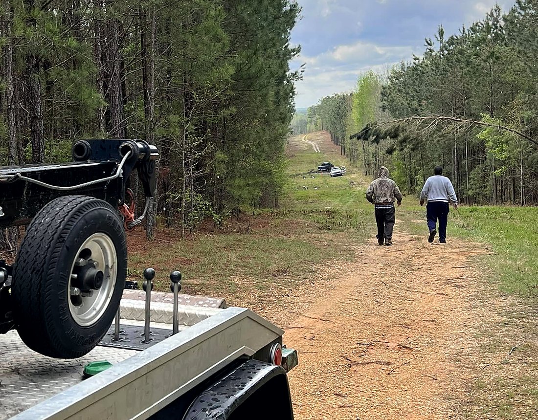 Rollback parked at the head of a dirt logging road, two men walking toward a vehicle in the distance